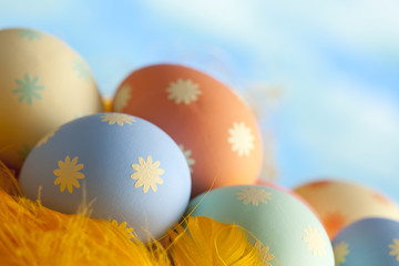 Colorful Easter eggs and yellow feathers on blue sky background