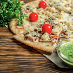 Pizza of veal in white sauce with pineapple and cherry tomatoes at wooden background