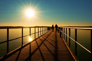 Morning in harbor. Tourists walk on pier above sea. Clear blue sky, smooth water level