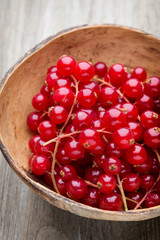 Redcurrant on a branch close to a wooden bowl.