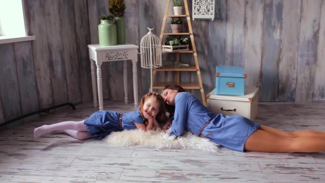 Beautiful happy family mother and daughter playing on the carpit tickle baby play with the baby smiling laughing vintage wood background same denim dresses