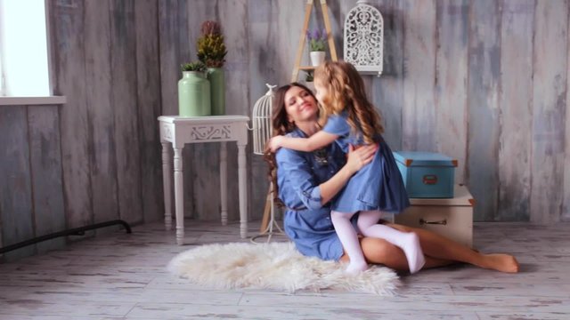 Beautiful happy family mother and daughter playing on the carpit tickle baby play with the baby smiling laughing vintage wood background same denim dresses