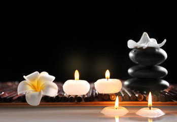 Spa still life with stones, candles and flowers in water on black background