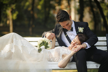 Beautiful bridal couple embracing on bench in the park