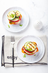 Grilled vegetables and cheese gratin stacked on a plate with fresh basil on white background