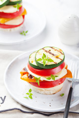 Grilled vegetables and cheese gratin stacked on a plate with fresh basil on white background