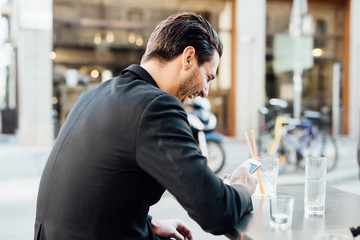 Rear view of young handsome man seated on a bar in the city cent