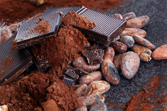 Chocolate pieces with cocoa beans and cocoa powder on a stone table