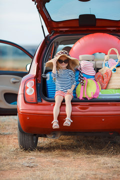 Little girl in straw hat sitting in the trunk of a car