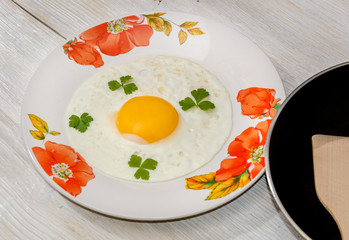 Fried eggs in a plate with a frying pan on a wooden background