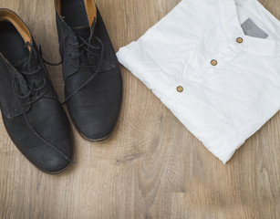 Men's black leather shoes and white shirts on wooden background.