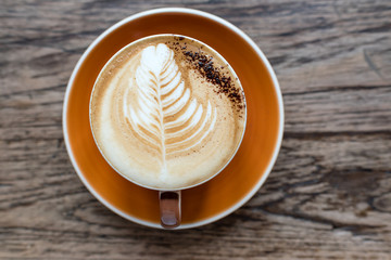 hot latte served in orange cup with latte art in fern shape