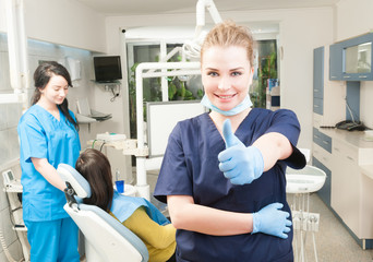 Obraz premium Confident smiling female dentist thumb up in her dental office