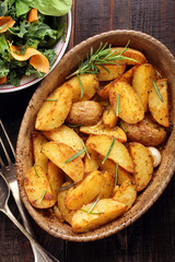 Roasted potato in brown bowl with fresh salad on wooden table