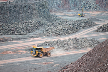 dumper truck driving through a quarry mine. excavator in backgro