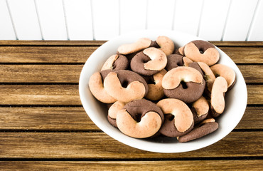 A dish full of cookies on brown wooden base and white wooden background