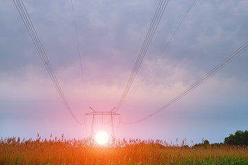 Open terrain, golf, huge electric poles of high voltage power lines at sunset wire stretching away to the horizon, the sun sitting down for poles at sunset, rising at dawn
