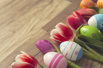 Photograph of a couple of colorful easter eggs with a bunch of tulips on wooden surface