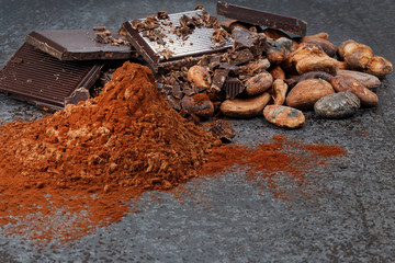 Chocolate pieces with cocoa beans and cocoa powder on a stone table