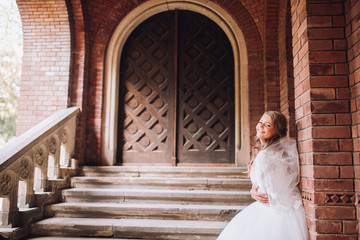 Obraz premium Beautiful young blond bride with bridal bouquet stands over ancient arch