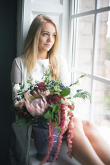 Florist at work: pretty young blond woman holds fashion modern bouquet of different flowers