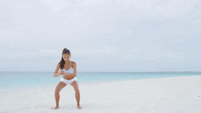 Fitness Asian woman on beach doing Pulse Squat pulses training and exercises training legs, butt, glutes and thighs as part of a full body core workout and active healthy lifestyle on beach. RED EPIC.