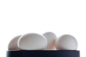 White eggs in a black bowl on white background from side