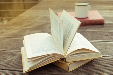Opened vintage book on the wooden table with old fashioned cup of tea. Side view. The toning.