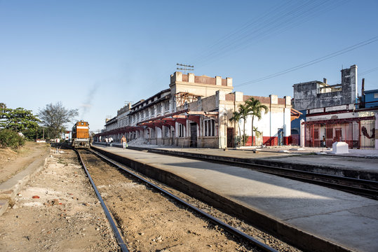 Kuba, Camagüey: Blick auf zentralen Bahnhof mit Diesellok, Schienen, Gebäude und blauem Himmel im Hintergrund  