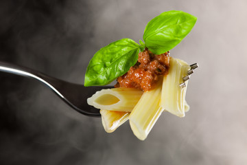 Fresh cooked pasta on fork with bolognese sauce and green basil