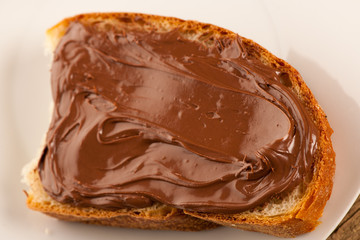 Slice of bread with sweet chocolate nougat spread on white plate
