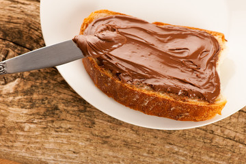 Slice of bread with sweet chocolate nougat spread on white plate