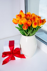 beautiful orange tulips and gift box on a window sill