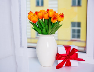 spring concept - beautiful orange tulips and gift box on a windo