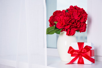 beautiful hydrangea flowers in vase and gift box on a window sil