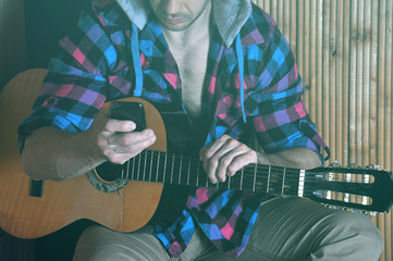 Fototapeta premium Hipster man hands holds phone and old crack guitar