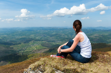 Naklejka na ściany i meble young woman sitting on top of a mountain and looking at the land