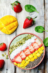 Spinach smoothie bowl with strawberries, coconut, mango, pumpkin