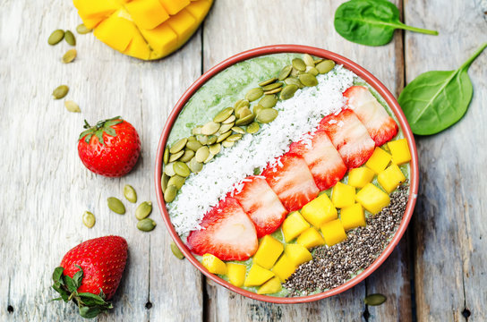 Spinach smoothie bowl with strawberries, coconut, mango, pumpkin