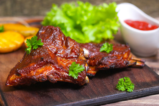 Delicious barbecued lamb ribs seasoned with a spicy basting sauce and served with chopped fresh herbs and potatoes on an old rustic wooden chopping board in a country kitchen