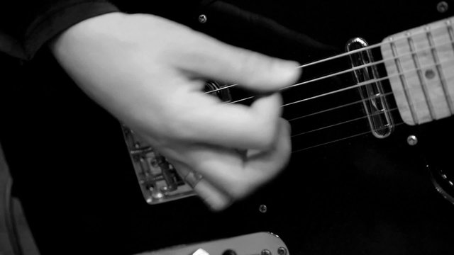 Musician playing electric guitar. Right hand striking the strings. Black and white. Close up. Slow motion.