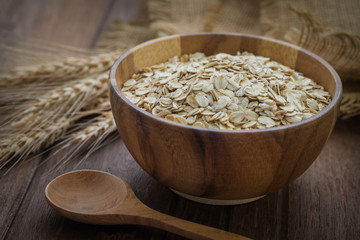 Oat flakes in wooden bowl and wheat