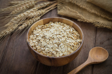 Oat flakes in wooden bowl and wheat