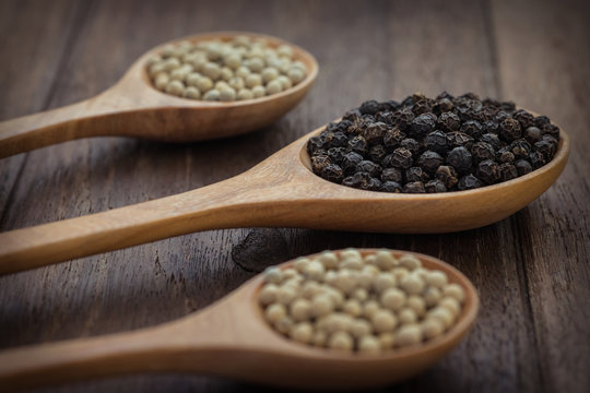 Black pepper and white pepper on wooden spoon