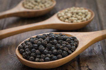 Black pepper and white pepper on wooden spoon
