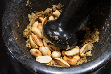 Mashing roasted peanuts in a black mortar, to cook Asian satay
