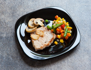 Pork steak on a black plate with vegetables