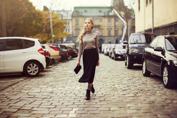 Street fashion concept: full body portrait of young beautiful woman walking in the city. Model looking aside. Toned and Filtered Photo.