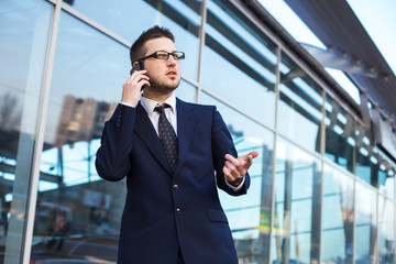 Attractive young businessman speak a cell phone, smiling. Standi