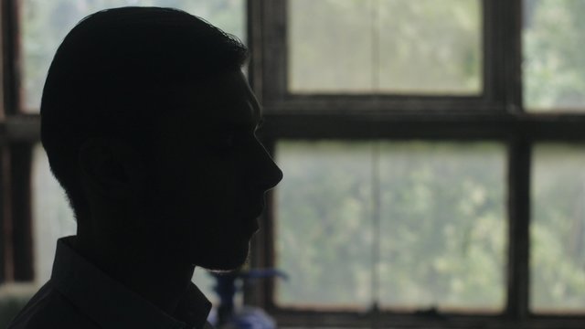 Silhouette of man head strat smoking a cigarette. Indoor. Window on background